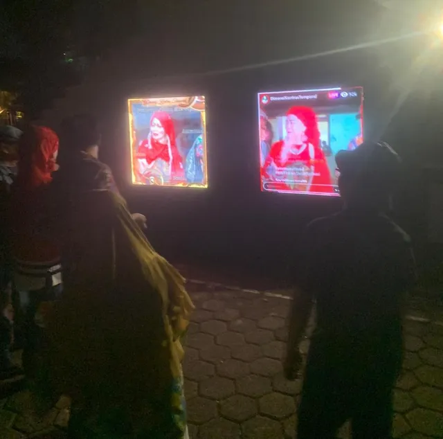 Pengunjung mengamati dua panel visual instalasi pada malam hari.