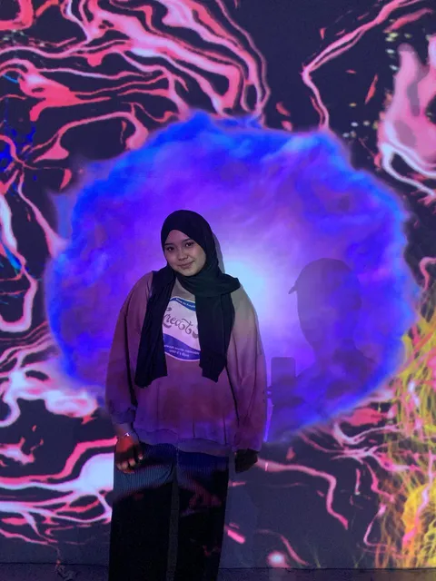 Pengunjung berpose di depan visual organik berwarna biru dan ungu.