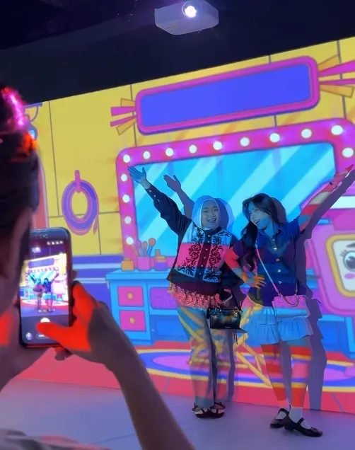 Pengunjung berpose di depan visual bertema perjalanan pada dinding instalasi.